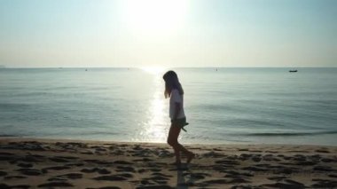 Genç dişi, kumlu sahil şeridi boyunca yalınayak yürüyor. Sabah güneşi altında dalgalar ve ufuklarla huzurlu deniz manzarasının tadını çıkarıyor.