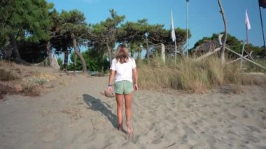 Dişi gezgin kumlu sahilde yalınayak yürüyor güneşli yaz tatilinde sakin okyanus ufkuna doğru ilerlerken geçici ayak izleri yaratıyor.