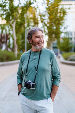 Klasik kameralı mutlu emekli adam şehir parkında yürüyor, boş zamanların ve aktif yaşlılar yaşam tarzının tadını çıkarıyor.