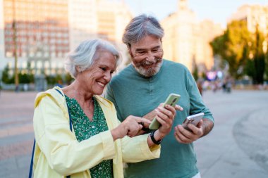 Gülümseyen yaşlı turistler, yeni bir şehri keşfederken akıllı telefonları birlikte kullanmaktan, fotoğraf ve mesajları paylaşmaktan keyif alıyorlar.