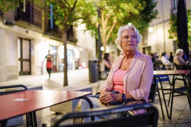 Düşünceli son sınıf öğrencisi kadın, kaldırımdaki kafede sakin bir anın tadını çıkarıyor, akşamları şehir hayatını gözlemliyor.