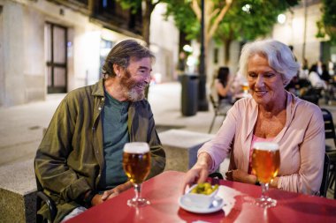 Gülümseyen son sınıf çifti açık bir kafede içki ve aperatiflerin tadını çıkarıyor, birlikte keyifli bir akşam geçiriyorlar.