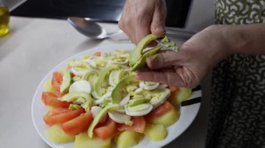 Şef titizlikle domates, patates ve haşlanmış yumurtalardan oluşan canlı bir salataya taze avokado dilimleri ekliyor. Renkli ve sağlıklı bir yemek oluşturuyor.
