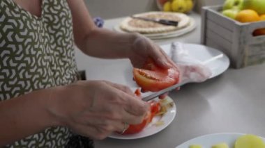 Olgun bir kadın evcil mutfakta olgun domates ve patates kesiyor, ev yapımı sağlıklı yemekleri keskin bıçakla taze malzemelerle hazırlıyor.