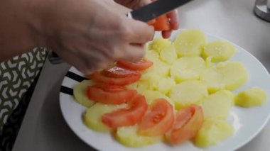 Domatesleri ve patatesleri dikkatlice dilimleyen yetenekli ev hanımı, mutfak düzeninde profesyonel mutfak hassasiyetinde ev yapımı sebze yemeği hazırlıyor.