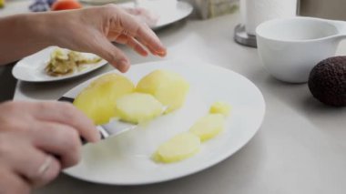Kadın aşçı, beyaz tabakta taze patatesleri profesyonel mutfak bıçağıyla dikkatlice dilimliyor. Yavaş çekim detaylarıyla mutfak ortamında kusursuz bir mutfak tekniği sergiliyor.