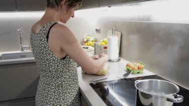 Pürüzsüz plastik poşetlerde taze patatesleri saklayan bir kadın, şık mutfak tezgahında dikilirken, dikkatli yemek muhafazasını yavaş çekimde yakalıyor.