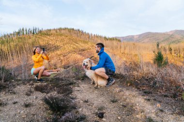 Yürüyüşçüler akıllı telefonlarıyla anılarını yakalıyorlar. Bir dağ ormanının güzelliğinin tadını çıkarırken aynı zamanda neşeli köpekleriyle birlikte.