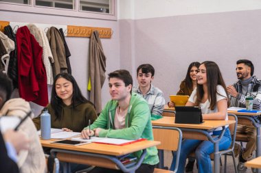 Hem geleneksel not defterlerini hem de elektronik tabletleri kullanarak sınıftaki bir dersi izleyen çok ırklı lise öğrencileri grubu.