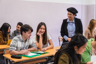 Lise öğretmeni ders sırasında öğrencilerine yardımcı oluyor, pozitif ve ilgi çekici bir öğrenme ortamı yaratıyor.