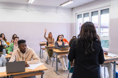 Çok ırklı öğrenciler el kaldırıyor ve bir lise sınıfında derslere katılıyor, eğitimlerine aktif olarak katılıyorlar.