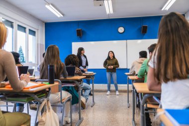 Asyalı lise öğrencisi modern bir sınıfta sınıf arkadaşlarının ve öğretmenlerinin önünde sunum yapıyor.