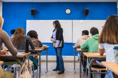 Bir sınıfta duran lise öğretmeni, sıralarda oturan öğrencilere çeşitli konularda bilgilendirici bir ders veriyor.