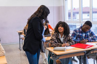 Sınav sırasında bir öğrenciye yardımcı olan lise öğretmeni, bir sınıf ortamında destek ve rehberlik sunar