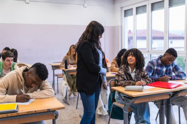 Bir sınıf ortamında yazılı sınavlarına odaklanan çok ırklı bir grup öğrenciyi denetleyen lise öğretmeni.