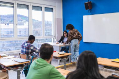 Lise öğrencileri ve öğretmenler, parlak ve modern bir sınıfta, işbirlikçi öğrenmeyi teşvik eden bir ders sırasında etkileşime girerler.