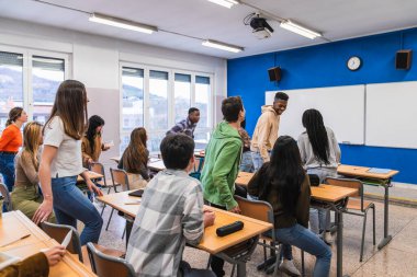 Sınıfta etkileşim halinde olan çok ırklı lise öğrencileri grubu, bazıları yürüme ve sohbet ederken diğerleri sıralarda oturuyorlar