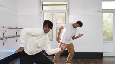 İki genç erkek hip hop dansçısı, parlak bir stüdyoda, yeteneklerini ve koordinasyonlarını sergileyerek dinamik bir gösteri yapıyorlar.