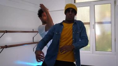 İki erkek dansçı, enerjik hip hop hareketlerini doğal ışıkla aydınlatılmış bir dans stüdyosunda sergiliyor.