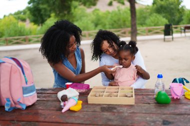 Mutlu Afro-Amerikan ailesi parkta eğleniyor, anne ve kızı besliyor, sağlıklı bir hayat sürüyor.