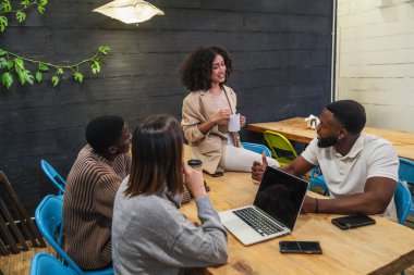 Bir grup genç profesyonel toplantı yapıyor, fikirleri tartışıyor ve modern bir çalışma alanında bir proje üzerinde birlikte çalışıyorlar.