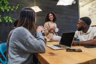 Farklı profesyonellerden oluşan çeşitli takımlar kahvelerini yudumlarken aynı anda şık bir çalışma alanında dizüstü bilgisayarlarla çalışıyorlar.