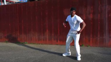 Enerjik genç erkek dansçı endüstriyel şehir ortamında paslı metal arka planıyla dinamik hip hop sokak dansı yapıyor.