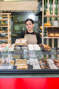 Pasta şefi elinde lezzetli hamur işleriyle dolu bir fırında kameraya gülümsüyor.