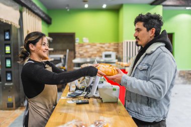 Gülümseyen fırıncı fırında yeni pişmiş bir somun ekmeği mutlu bir müşteriye uzatıyor, harika bir servis anı yaratıyor.