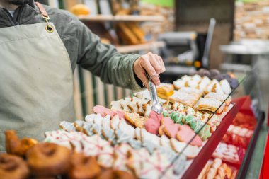 Fırıncı renkli Noel kurabiyeleri düzenlemek için maşa kullanıyor ve bir pastanede sergileniyor.