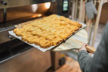 Baker, profesyonel bir fırından altın sarısı palmiyelerden bir tepsi alıyor ve fırını tatlı bir aromayla dolduruyor.