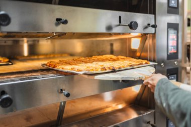 Baker, profesyonel bir fırından bir tepsi altın kahverengi hamur işi alıyor ve fırını lezzetli aromalarla dolduruyor.