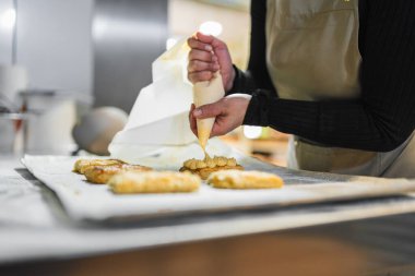 Pasta şefinin ellerini boru torbasıyla kapayın, pastanede tatlı kremayla doldurun.