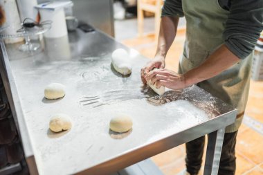 Fırıncı ustalıkla paslanmaz çelik bir masada hamur yoğurur, profesyonel bir mutfak ortamında ekmek ve hamur işleri hazırlar.