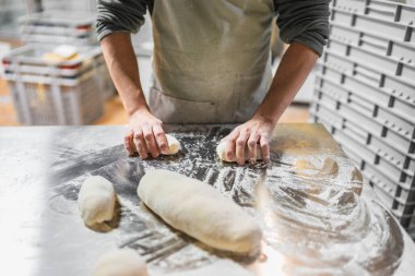 Fırıncı ekmek ve hamur işleri için hamur hazırlıyor, profesyonel bir fırın mutfağında paslanmaz çelik bir masada un ile çalışıyor.