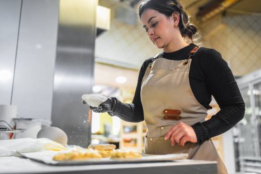 Profesyonel fırıncı, bir tepsi lezzetli pastaya şeker serpiyor. Ticari bir mutfakta çalışıyor.