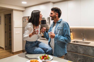 Genç çift romantik bir anın tadını çıkarıyor, el ele tutuşuyorlar ve modern mutfaklarında kahve içiyorlar.
