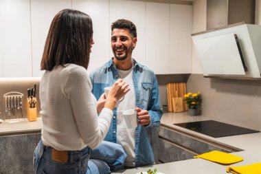 Genç çift, modern mutfaklarında kahve içerken bir yandan da sohbet ediyor. Birbirinin dostluğundan ve sıcak atmosferden keyif alıyorlar.