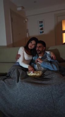 Romantik çift evde film gecesinin tadını çıkarıyor, patlamış mısırlarını paylaşıyorlar ve kanepenin altında sarılıyorlar.