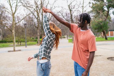 Genç, çok ırklı bir çift el ele tutuşuyor ve etrafta dönüyor. Parkta kaygısız bir günün tadını çıkarıyorlar.