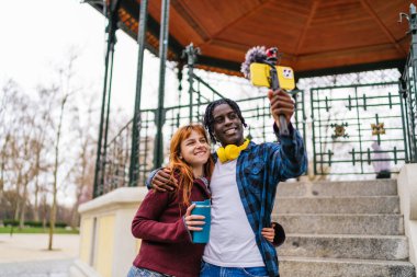 Genç çok ırklı vlogger çifti, akıllı telefon ve jimnastik aleti ile parkta video içeriği kaydediyor.