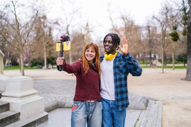 Sosyal medya için parkta akıllı telefon ve hoparlörle video kaydeden mutlu çoklu etnik video kaydediciler.