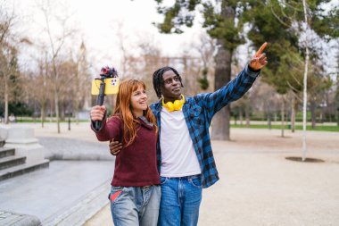 Genç, çok ırklı bir çift parkta volta atıyor ve akıllı telefon kullanarak eğleniyor.