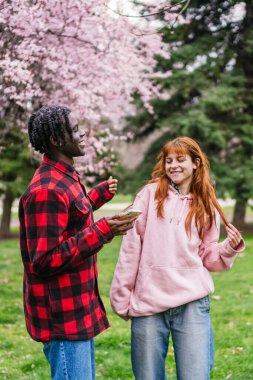 Pembe çiçekler ve yeşilliklerle çevrili neşeli bir çift parkta dans ediyor. Mutluluk ve neşe kavramı.