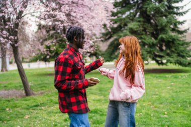 Genç bir adam, canlı bir parkta kızıl saçlı bir kadınla dans ederken telefonunu tutuyor. Eğlence anlayışı.