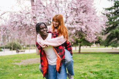Genç, çok ırklı bir çift baharda çiçek açan ağaçlarla dolu bir parkta eğleniyor.