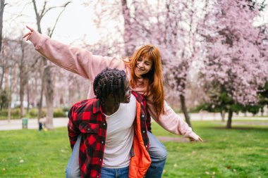Genç, çok ırklı bir çift, çiçek açan ağaçlarla dolu bir parkta, aşkı ve çeşitliliği kutluyor.