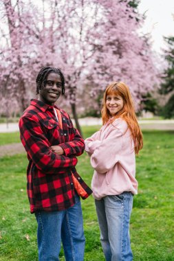 Mutlu çok ırklı çift, pembe ağaçlarla çevrili bir parkta canlı bir bahar gününün tadını çıkarıyor. Birlikte sevgi ve neşe saçıyorlar.