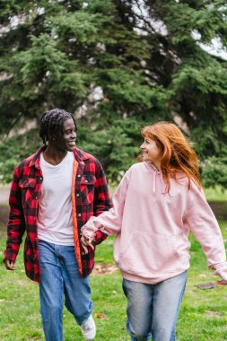 Genç, çok ırklı bir çift el ele tutuşup parkta yürüyorlar ve dışarıda romantik bir anın tadını çıkarıyorlar.