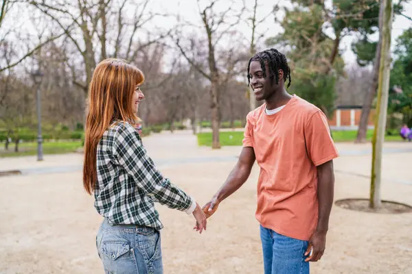 Genç, çok ırklı bir çift parkta el ele tutuşuyor ve gülümsüyor. Birlikte romantik bir anın tadını çıkarıyorlar.